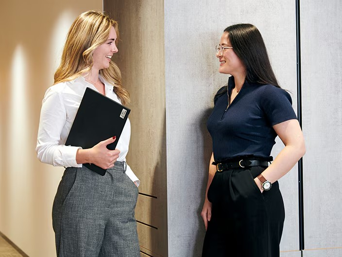 Two professional women in business attire standing together, showcasing teamwork and collaboration in a business environment