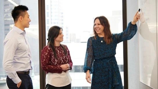 Three individuals engaged in discussion, standing in front of a whiteboard filled with notes and diagrams