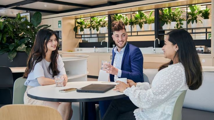 Two female and on male Allianz Colleague sitting on a table drinking water and talking to each other.