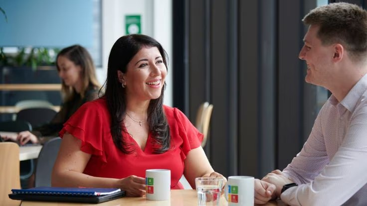A man and woman engaged in conversation while seated at a table in a professional office setting