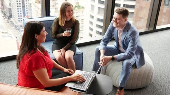 A casual office scene featuring three people comfortably sitting on bean bags, discussing ideas in a relaxed atmosphere