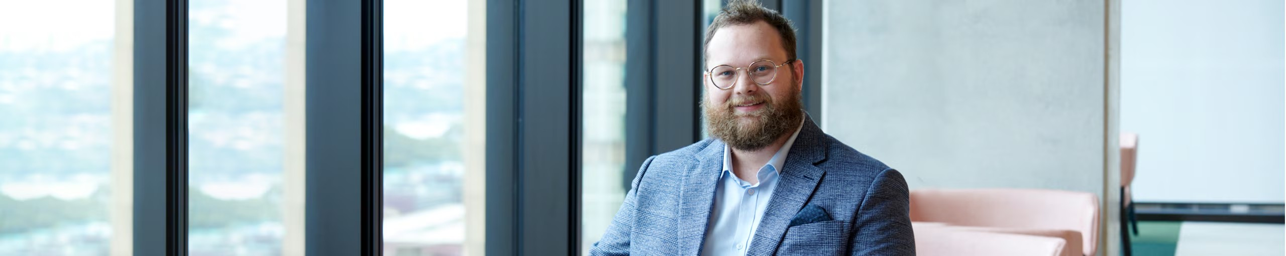 A professional with glasses and a beard seated on a couch