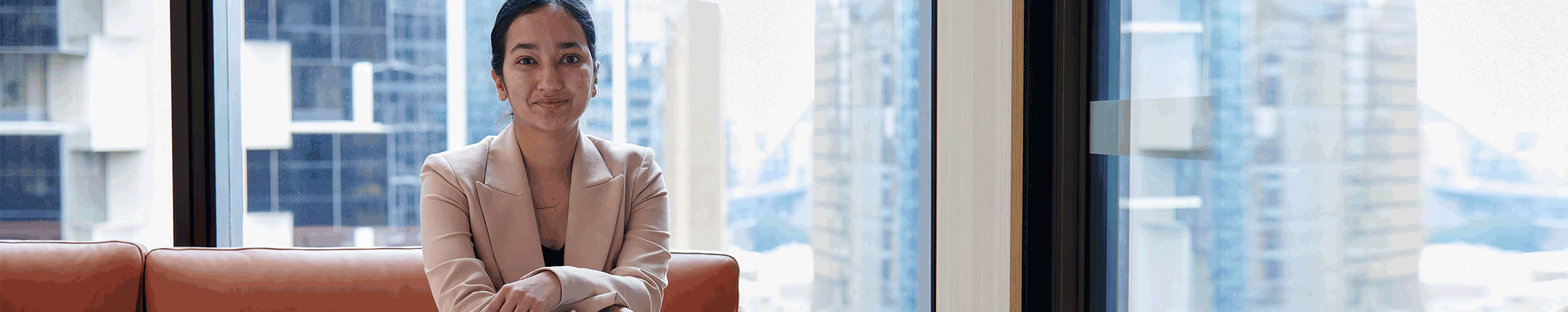 A woman seated on a couch, gazing out of a window, with natural light illuminating the room
