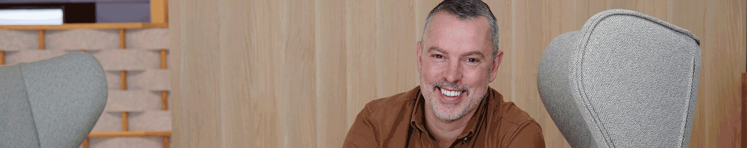 A man sits on a couch, smiling warmly and appearing relaxed