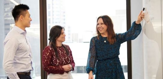 Three individuals standing in front of a whiteboard, engaged in discussion or presentation