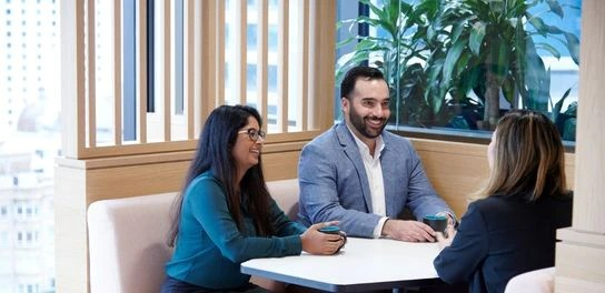 Three individuals engaged in discussion while seated at a table in a professional office environment