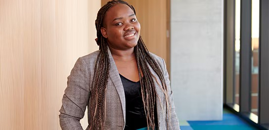 A woman with braids stands confidently in front of a textured wall
