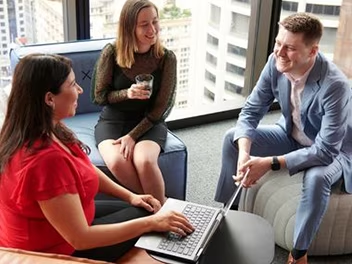 A casual office scene featuring three people comfortably sitting on bean bags, discussing ideas in a relaxed atmosphere