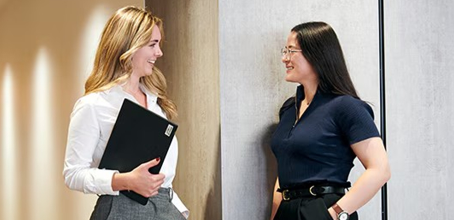 Two professional women in business attire standing together, showcasing teamwork and collaboration in a business environment