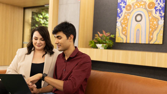 Steph and Shubham seated on a couch, engaged with a laptop in front of them, sharing a moment of collaboration