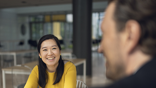 Woman in a yellow sweatshirt smiling at colleague