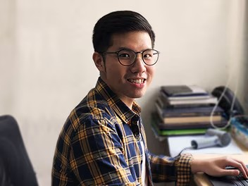 A colleague using a laptop, smiling at the camera while engaged in their work. They look cheerful and focused in their environment.