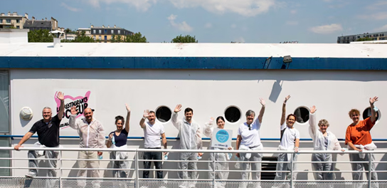 Groupe de personnes saluant et souriant à la caméra, profitant de leur temps ensemble.