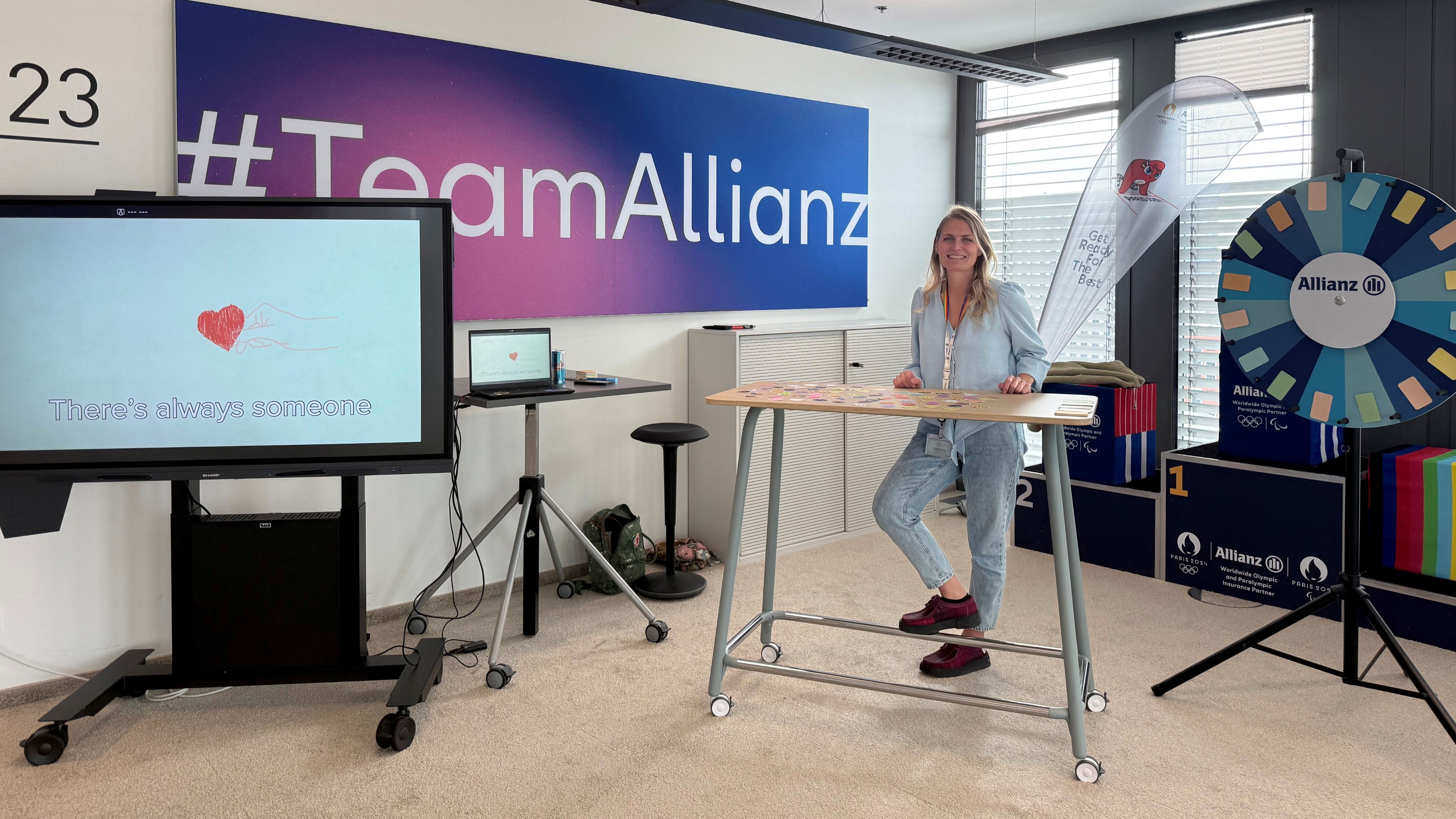 Woman standing in front of desk and screen shows text "there is always someone"