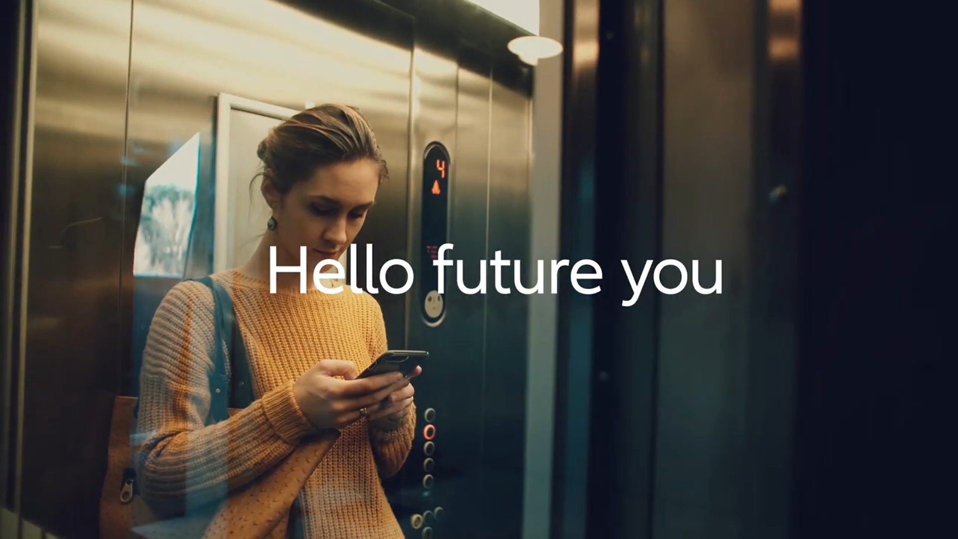 Woman using mobile phone while standing in a lift with text overlayed: "Hello future you"