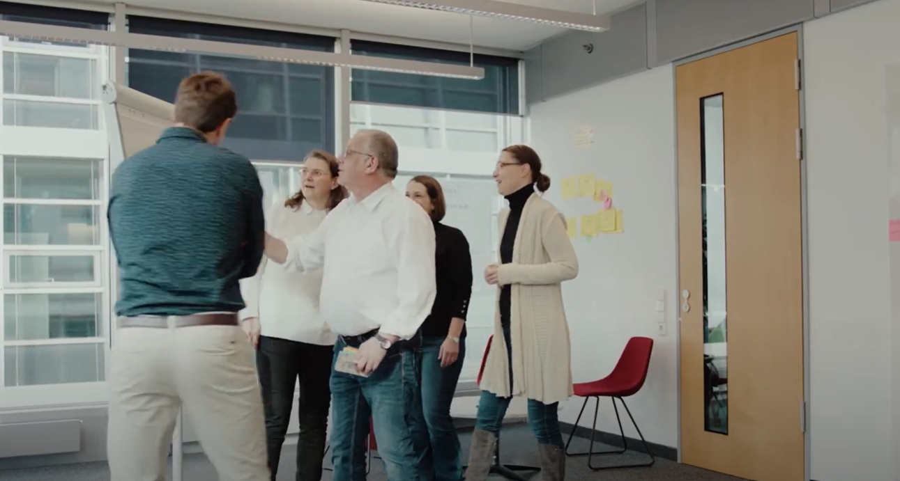 Allianz Mitarbeiter gemeinsam in einem Meetingraum bei einem Workshop mit Flipcharts und Stühlen