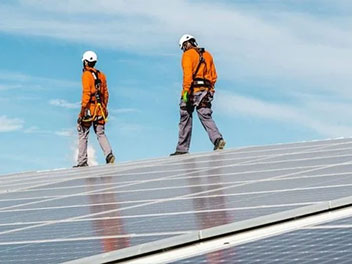 Two workers inspecting photovoltaic panels on a sunny rooftop.