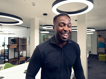 A man in a black shirt is smiling while standing in a modern office space