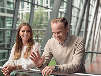 Two colleagues in a modern office environment, and both appear engaged in their discussion.