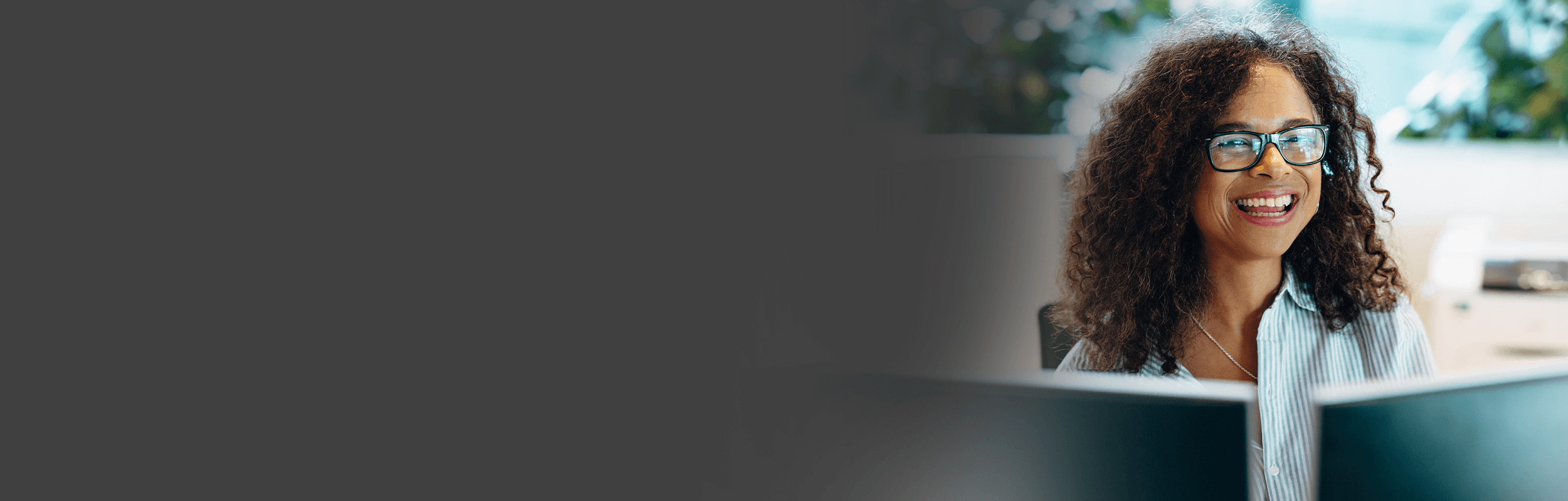 Smiling woman wearing glasses sitting at a desk with dual monitors