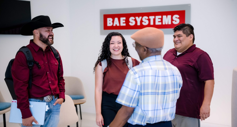 Four BAE Systems colleagues talk in a lobby. 