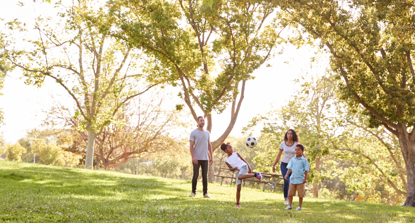 Family plays soccer in the park.