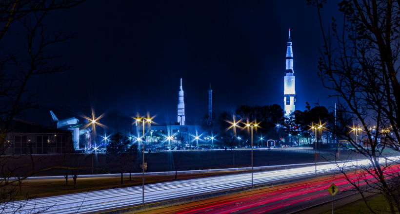  Long-exposure night view of traffic passing the U.S. Space & Rocket Center in Huntsville, with illuminated rockets rising above the highway.
