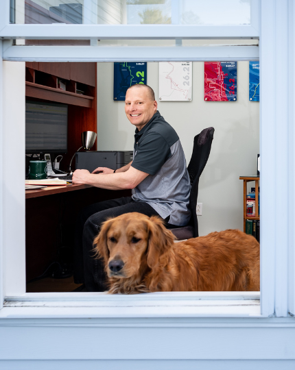 Greg, an engineering director, smiles for a photo in his home office. His golden retriever Luna, stands in the foreground.