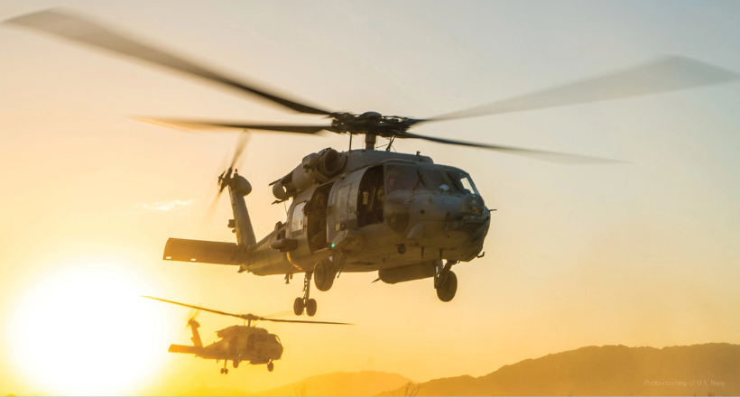 Two military helicopters flying in sunset.