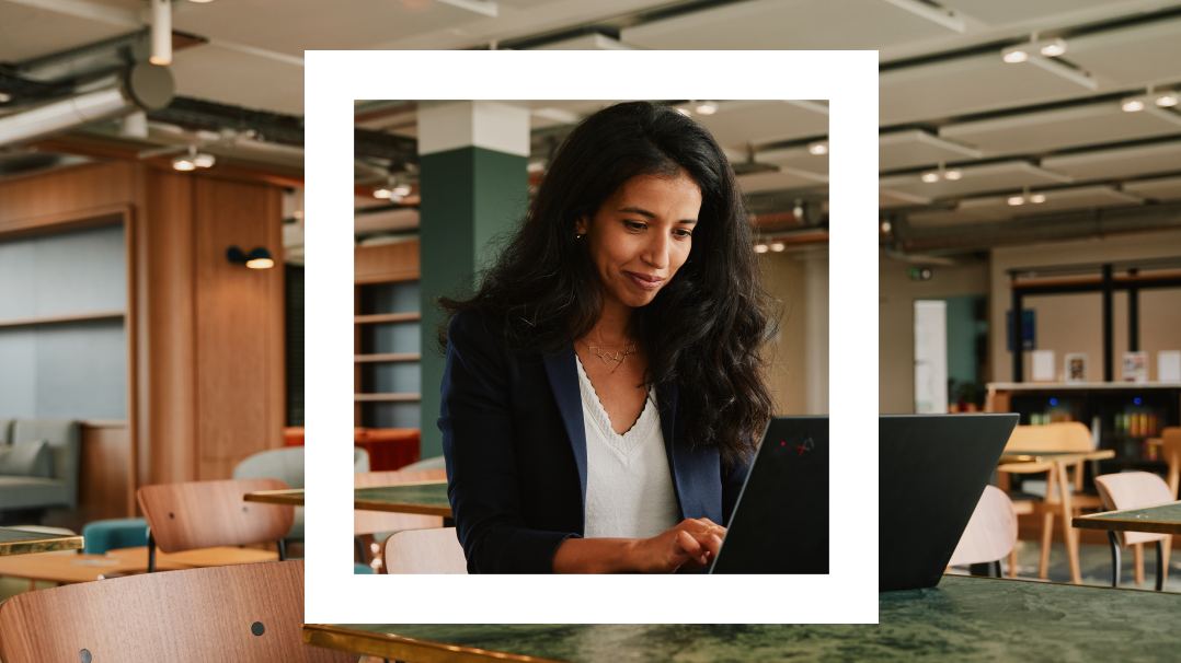  The image features a young woman in a business casual outfit, concentrating on her laptop in a modern office environment. The background shows a stylish workspace with contemporary furniture and a relaxed, open plan layout. The office is bright and colorfully decorated with a mix of wooden fixtures and vibrant green plants, enhancing the ambiance of a productive yet comfortable workplace. The woman is framed within a white border, giving the photograph a polished, focused look.