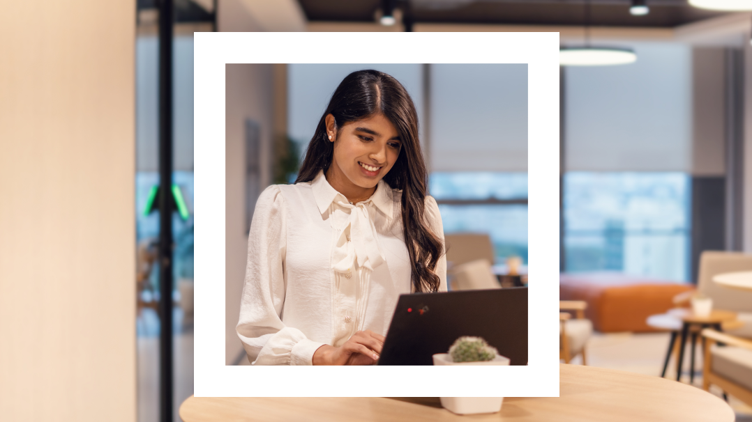 The image features a young woman focused on her laptop, framed within a white border against a modern office background. She is dressed in a stylish white blouse with a bow tie at the neck, and her expression is one of concentration and engagement. The office environment is warmly lit and furnished with contemporary decor.