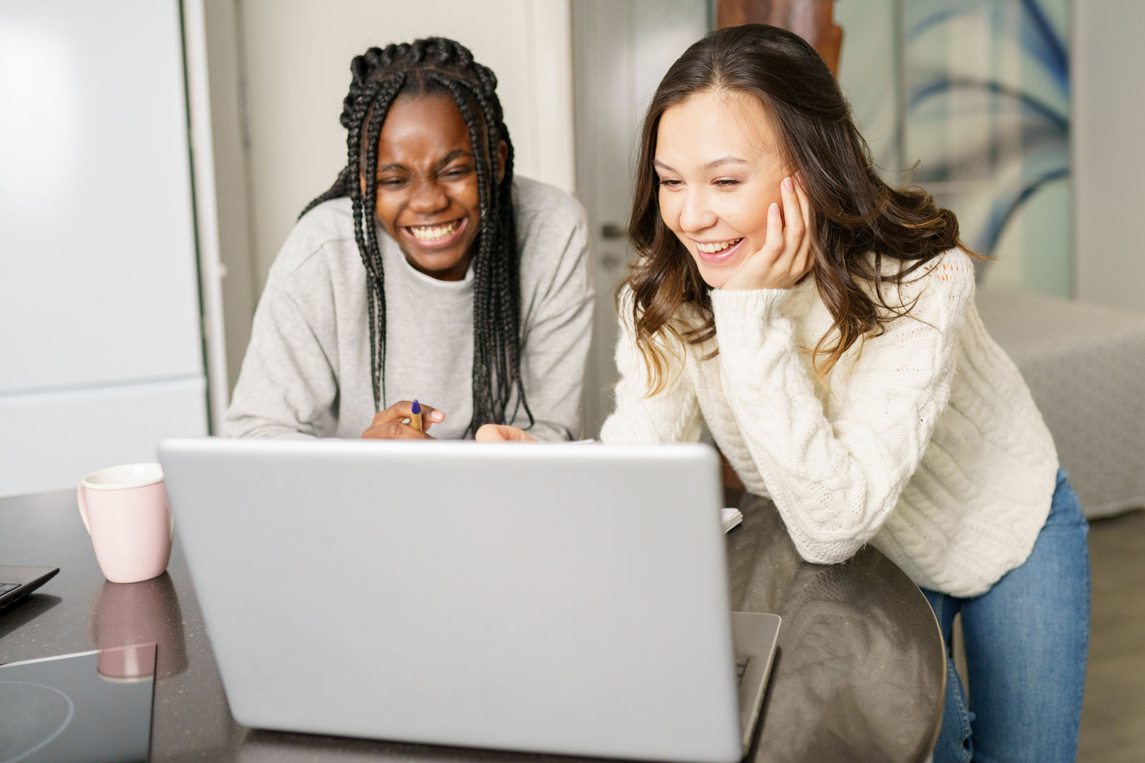 Twowomensmilingwhileusingcomputerontable3