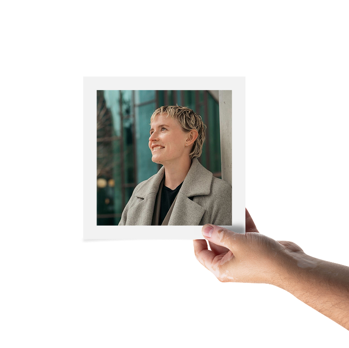 A hand is holding a framed photo of a woman smiling.  She is wearing a black top under a gray blazer jacket.