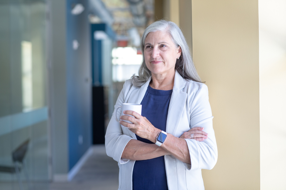 Person standing in a hallway holding a coffee cup.