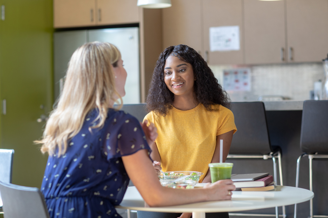 Two colleagues sitting at a table having a conversation in a workplace break area.
