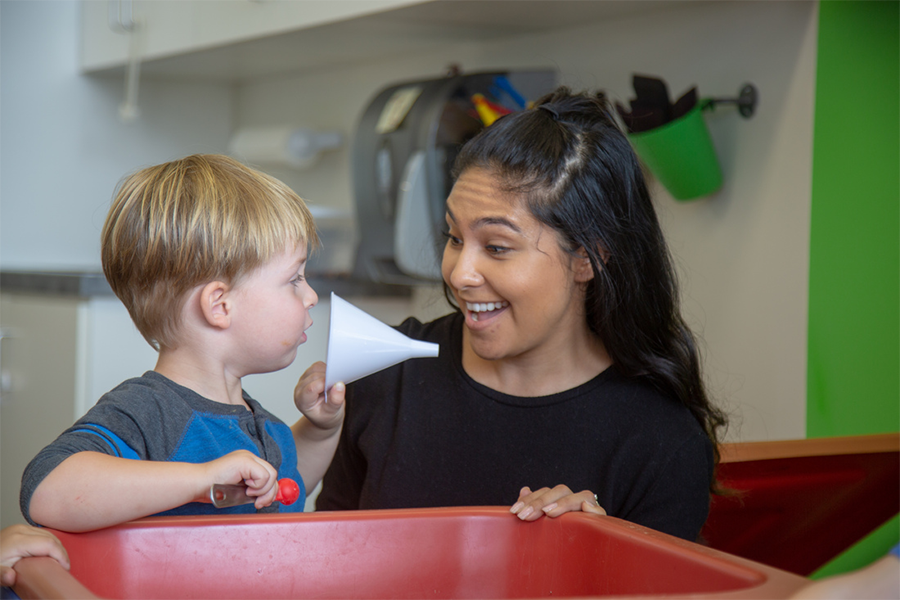Adult and child playing with a funnel at a sensory table.
