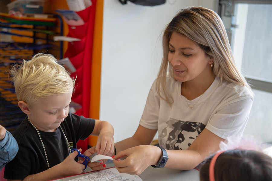 Adult helping child cut paper during a craft activity.