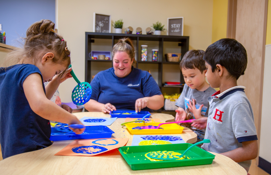Children participating in a painting activity using colorful trays and textured tools.