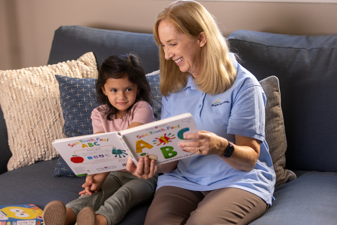 Caregiver reading an ABC book with a child on a couch.