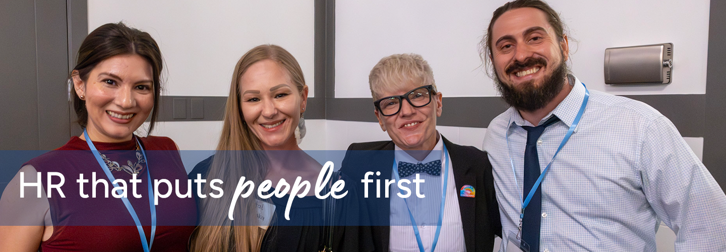 Four individuals standing together indoors wearing business attire and blue lanyards, with text overlay reading “HR that puts people first.