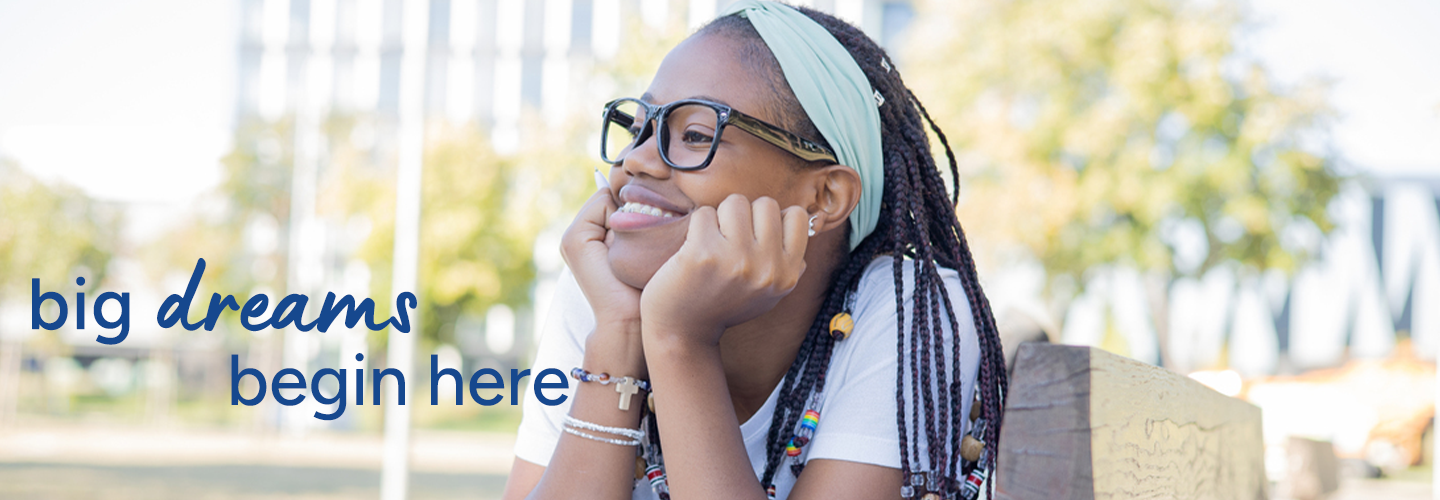 Person sitting outdoors on a wooden bench, wearing a white shirt and colorful beaded braids, with a light green headband. Text on the image reads: “big dreams begin here.”