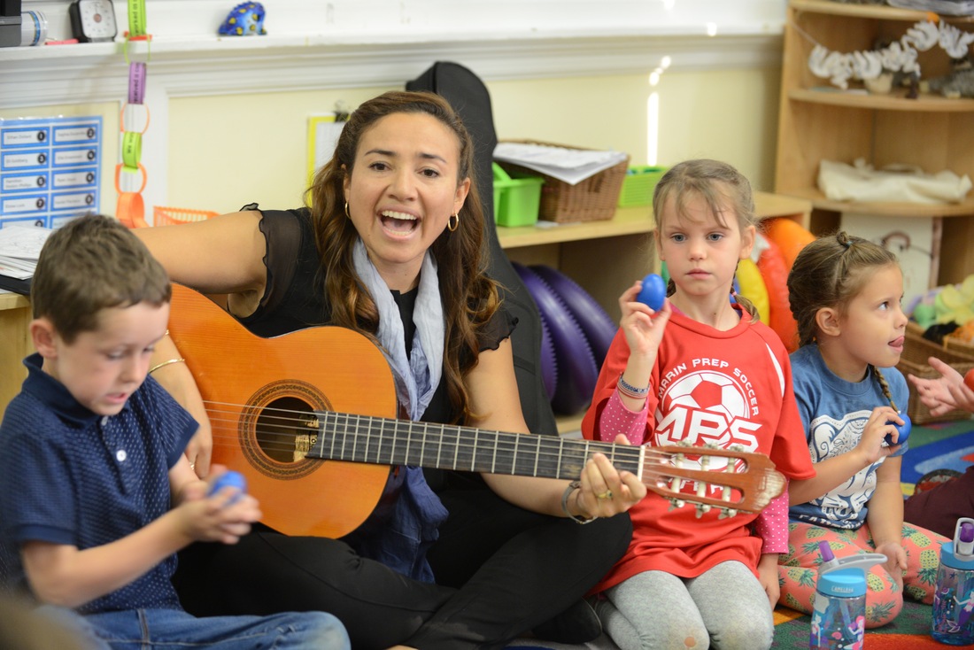 Adult playing guitar with children during a music activity.