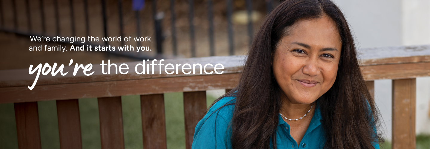 A woman with long hair smiles warmly while sitting on a wooden bench. The background is a blurred outdoor setting. The text reads, "We're changing the world of work and family. And it starts with you. You're the difference.