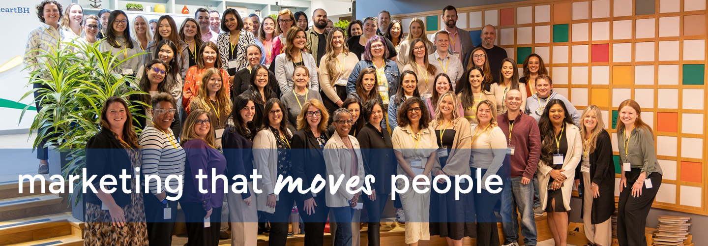A large group of people standing together in a brightly lit office space with colorful wall panels and plants, with text overlay reading “marketing that moves people.”
