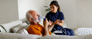A health care professional in navy blue scrubs checks a patient's blood pressure while providing care during a home health visit.