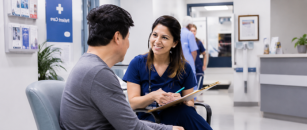 Patient Care Technician smiling while speaking with a patient in a clinical setting, demonstrating compassionate, patient-centered care and building meaningful connections.