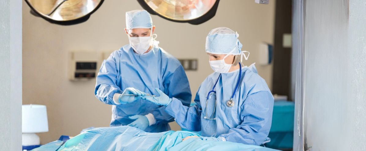 Two surgical team members in protective surgical attire and masks working together in an operating room during a patient procedure, representing surgical services and collaborative patient care.