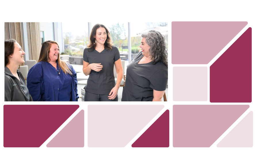 Four health care professionals smile and talk together in a bright clinical setting, highlighting teamwork and collaboration.