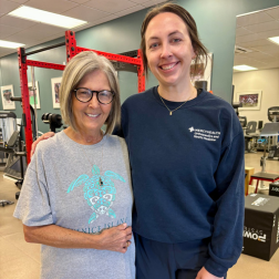 Patient and health care professional smiling in a physical therapy gym with equipment in the backgroundx252px2