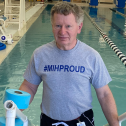 Stephen C. in a rehabilitation pool wearing a “#MIHPROUD” shirt and holding therapy equipment